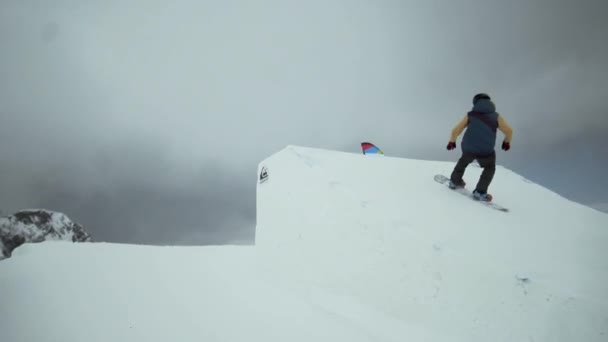 Σότσι, Ρωσία - 31 Μαρτίου 2016: Snowboarder κάνει ακραία άλμα από τραμπολίνο στο χιονισμένο βουνό. ουρανός γκρι σύννεφο. Χιονοδρομικό κέντρο — Αρχείο Βίντεο