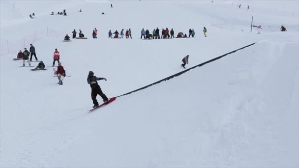 Sochi, Rusko - 31 března, 2016: Snowboardista se, jezdit na můstek, slide na železnou stezkou na svahu. Přepínač na šířku. Zasněžené hory. — Stock video