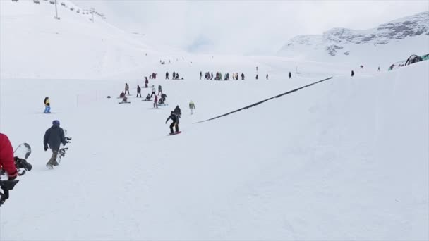 Sotschi, Russland - 31. März 2016: Snowboarderfahrt auf dem Sprungbrett, Rutschpartie auf dem Eisenpfad am Hang. Landschaft. Schneebedeckte Berge. Wettbewerb — Stockvideo