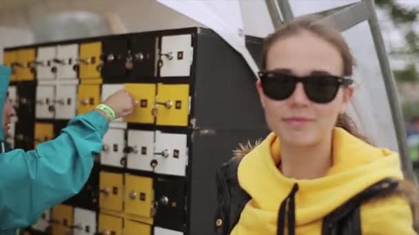 SAINT PETERSBURG, RUSSIA - JULY 16, 2015: Girl in sunglasses smile. Boy put things in little luggage room, close lock on summer festival. — Stock Video