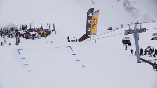 Sochi, Rusko - 29 března, 2016: Snowboardista helmu skok od odrazový můstek na lyžařské středisko, flexe nohy ve vzduchu. Zasněžené hory. Lidé — Stock video