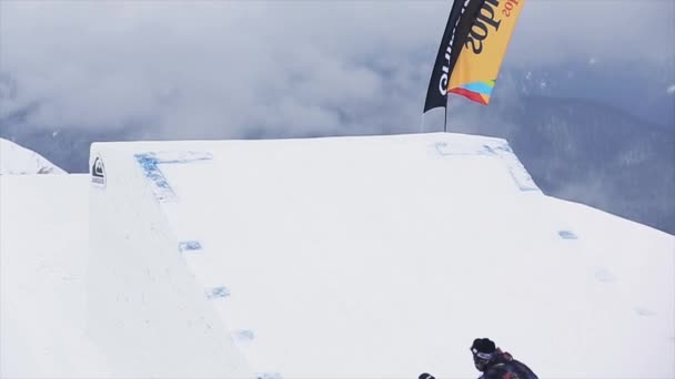 SOCHI, RÚSSIA - 29 de março de 2016: Snowboarder em salto uniforme do trampolim, vire. Montanhas nevadas. Desporto extremo. Paisagem — Vídeo de Stock