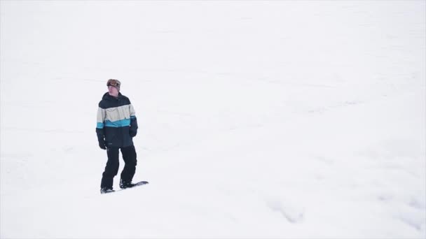 SOCHI, RUSIA - 29 DE MARZO DE 2016: Paseo de snowboarder en trampolín, salto. Paisaje de montañas. Cielo gris. Concurso. Banderas. Extremo. — Vídeo de stock