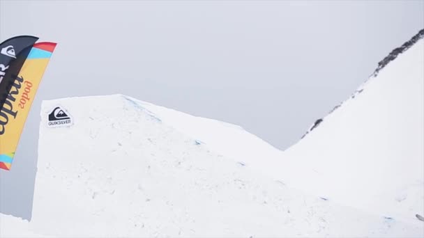 Sochi, Rusko - 29 března, 2016: Snowboardista skočit z trampolíny, chytni desky ve vzduchu. Krajina hor. Šedá obloha. Soutěž — Stock video