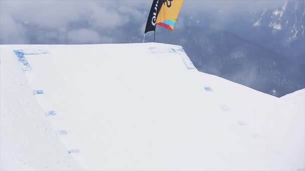 SOCHI, RUSIA - 29 DE MARZO DE 2016: Snowboarder en salto uniforme desde trampolín, hacer voltear en el aire, agarrar el tablero. Montañas nevadas. Extremo. — Vídeos de Stock