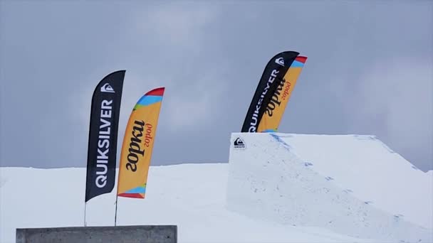 Soči, Rusko - 29 března, 2016: Snowboardista v jednotných skok z odrazový můstek, aby převrátí ve vzduchu. Zasněžené hory. Přepínač na šířku. Extrémní — Stock video