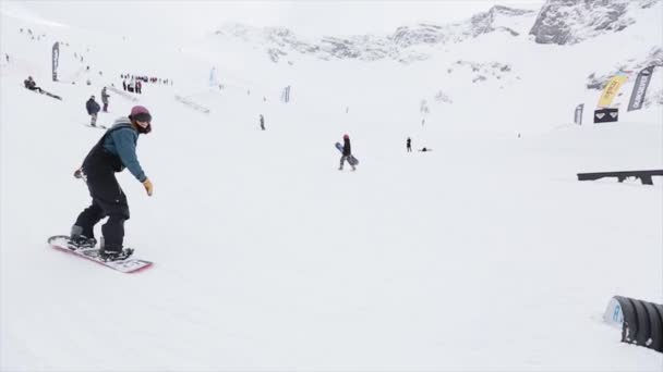 Sochi, Rusko - 31 března, 2016: Snowboardista jízdu na odrazový můstek, aby kousek. Přepínač na šířku. Zasněžené hory. Soutěž. Lidé. Lyžařské středisko — Stock video