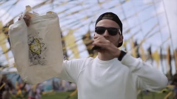 SAN PETERSBURG, RUSIA - 16 DE JULIO DE 2015: Hombre con gorra, gafas de sol, con micrófono show bolsa blanca a la gente en el festival de verano. Entretenimiento . — Vídeo de stock