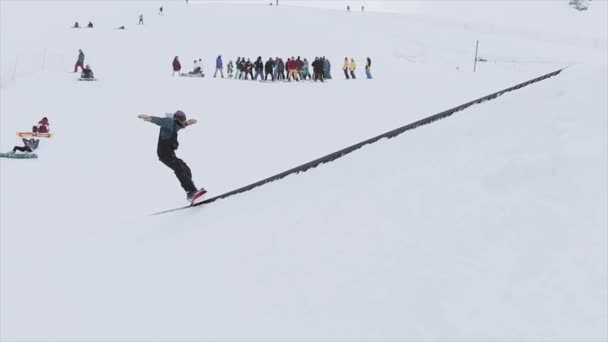 SOCHI, RUSIA - 31 DE MARZO DE 2016: Paseo de snowboarder en trampolín para volver a deslizarse por el sendero de hierro. Paisaje. Montañas. Concurso. Gente — Vídeos de Stock