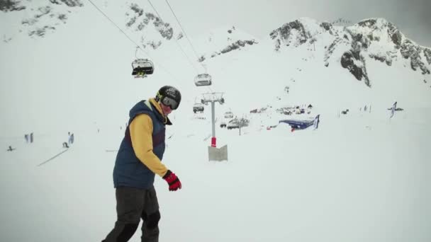 SOCHI, RUSIA - 31 DE MARZO DE 2016: Paseo en snowboarder en la ladera de la montaña nevada. Mira en cámara, salta del trampolín. Estación de esquí — Vídeos de Stock