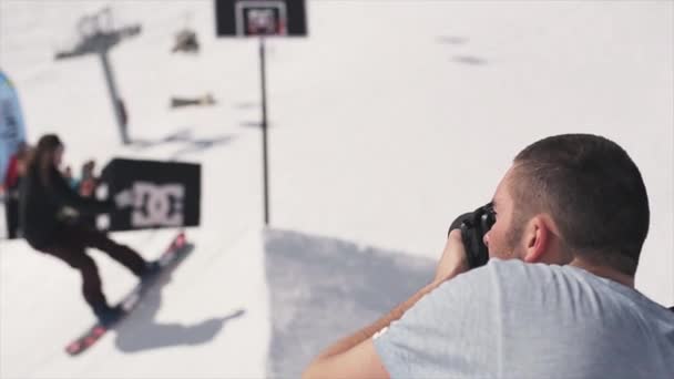 Sochi, Rusko-1, 2016: kameraman skáčou na snowboardistu z odrazový můstek za basketbalovým košíkem. Slunce — Stock video
