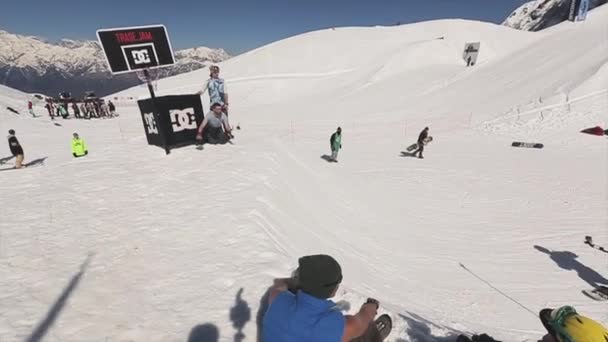 Sotschi, Russland - 1. April 2016: Snowboarder machen Sprung auf Sprungbrett werfen Schneeball in Korb. Menschen. blauer Himmel. — Stockvideo