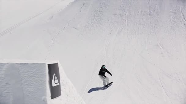 Сочі, Росія - 1 квітня 2016: Сноубордист стрибках з трампліну зробити фліп в повітрі. Засніжених гір. Сонячно. Синє небо. Екстрім — стокове відео
