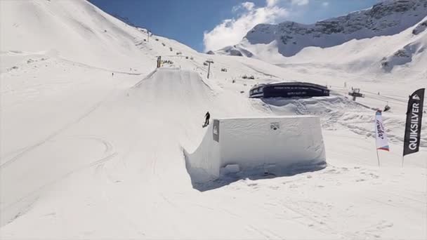 SOCHI, RÚSSIA - 1 de abril de 2016: Snowboarder jump on springboard. Paisagem de montanhas nevadas. Céu azul. Estância de esqui. Dia ensolarado — Vídeo de Stock