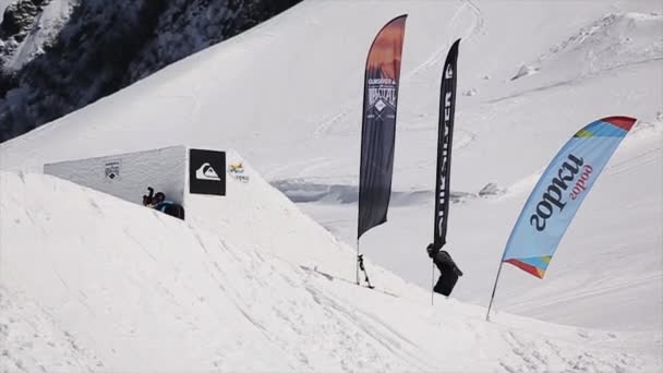 SOCHI, RUSSIA - APRIL 1, 2016: Snowboarder jump from springboard make several full flips in air. Landscape snow mountains. Blue sky — Stock Video