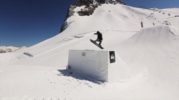 Sochi, Rusko - 1. dubna 2016: Snowboardista skok od odrazovým můstkem celé převrátit ve vzduchu. Zasněžená krajina. Modrá obloha — Stock video