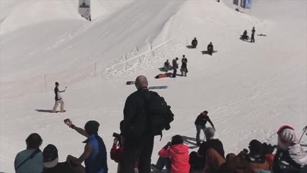 SOCHI, RUSSIE - 1er AVRIL 2016 : saut en snowboard depuis un tremplin tournant dans l'air. Les gens. Montagnes enneigées . — Video