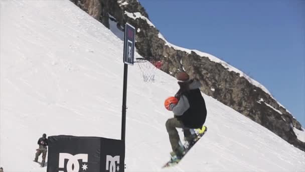 Soči, Rusko - 1. dubna 2016: Snowboardista skoku hodit míč do basketbalového koše. Slunečný den. Krajina hor — Stock video