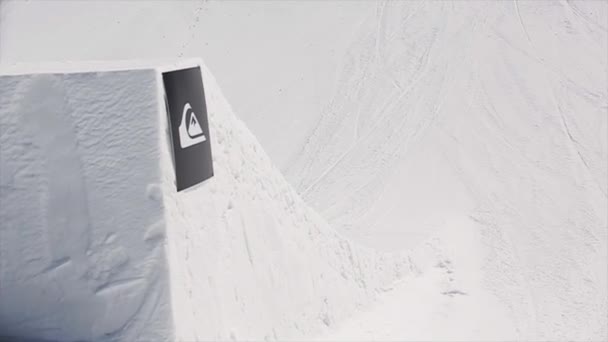 SOCHI, RUSSIA - APRILE 1, 2016: Snowboarder salto in alto dal trampolino di lancio fare capovolgere in aria, fallendo. Montagne innevate. Soleggiato. Cielo blu — Video Stock