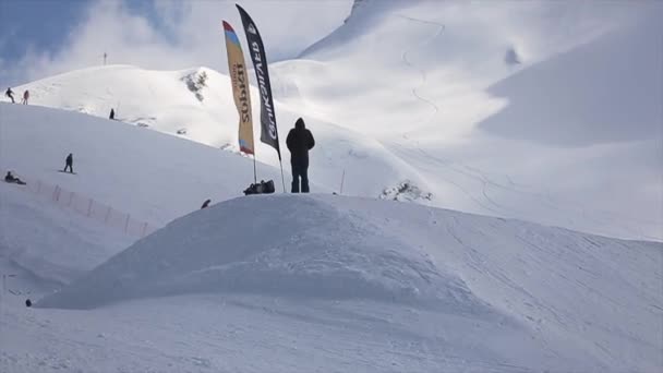 Sochi, Rusko - 1. dubna 2016: Snowboardista vysoký skok od odrazový můstek, jezdit na svahu. Zasněžené hory. — Stock video