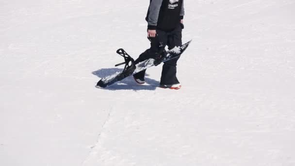 SOCHI, RUSSIA - 1 APRILE 2016: Snowboarder cammina sul pendio. Tieni lo snowboard in mano. Località sciistica. Giornata di sole . — Video Stock
