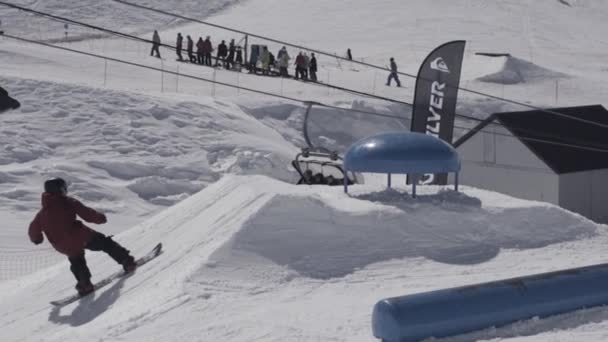 Сноубордист совершает экстремальный прыжок на трамплине в снежных горах. Экстремальный трюк. Солнечный день. Люди — стоковое видео