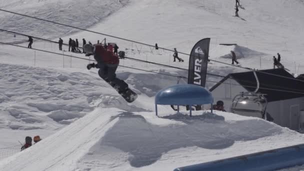 Snowboarder, hogy ugrik a lejtőn ugródeszka a havas hegyek extrém flip. Süt a nap. Sífelvonó — Stock videók