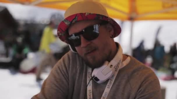 СОЧИ, РОССИЯ - 1 апреля 2016 года: Dj in hat, sunglasses spinning at turntable on ski resort. Держите мяч в руках . — стоковое видео