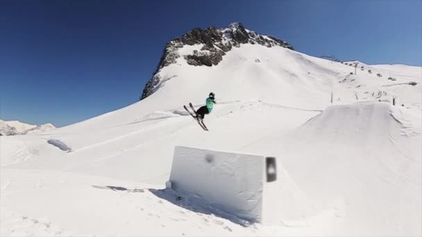 Sochi, Rusland - 1 April 2016: Buigt skiër sprong van de Springplank voeten in de lucht. Besneeuwde bergen. Zonnige dag. Blauwe hemel. Cameraman — Stockvideo