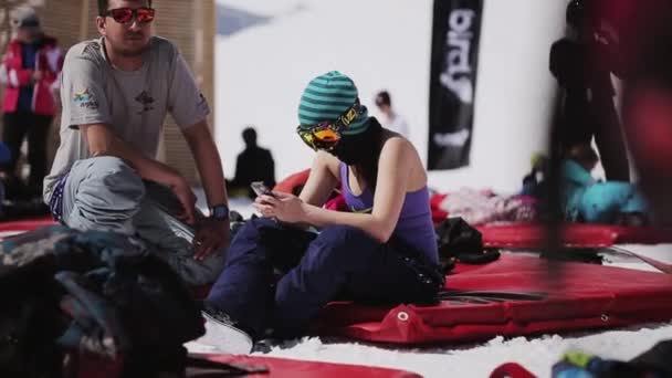 SOCHI, RUSIA - 1 DE ABRIL DE 2016: Niña y hombre se sientan en un colchón inflable. Estación de esquí. Encamp. Soleado. Gafas de sol — Vídeos de Stock
