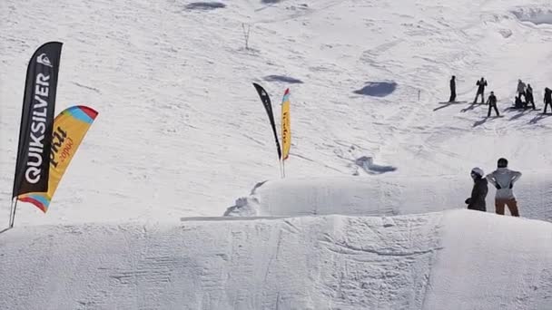 SOCHI, RUSIA - 1 DE ABRIL DE 2016: Salto de snowboard desde trampolín. Montañas nevadas. Día soleado. Gente. Deporte extremo. Pendientes — Vídeo de stock