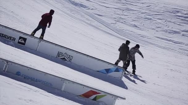 СОЧИ, РОССИЯ - 2 апреля 2016 года: Сноубордисты скользят по склону горнолыжного курорта. Езжай по рельсам, делай трюки. Солнечный день . — стоковое видео