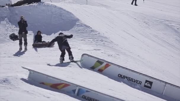Sochi, Oroszország - április 2-án, 2016: Snowboardos, hogy visszaesik a vasúti, a ski resort. Süt a nap. Hegyek. Az emberek. — Stock videók