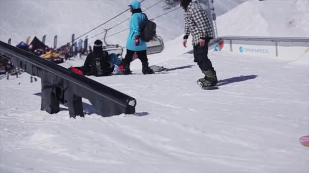 SOCHI, RÚSSIA - 2 de abril de 2016: Snowboarder slide on rail on ski resort. Ensolarado. Montanhas nevadas. Cameraman — Vídeo de Stock
