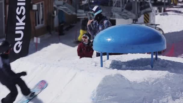 Sotschi, Russland - 2. April 2016: Snowboarder springen über blauen Kicker, berühren. Sonnig. Skigebiet. Schneebedeckte Berge. — Stockvideo