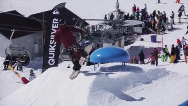 SOCHI, RUSSIE - 2 AVRIL 2016 : Snowboarder jump over blue kicker. Ensoleillé. Station de ski. Montagnes enneigées. Les gens — Video