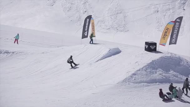 Sotschi, Russland - 2. April 2016: Snowboarder springen vom Sprungbrett auf Skigebiet. Sonnig. Schneebedeckte Berge. Reiten — Stockvideo