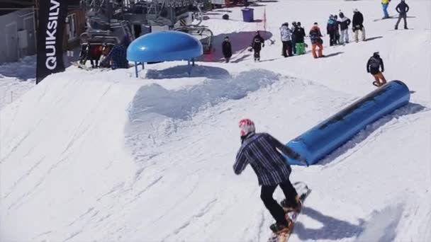 Sochi, Oroszország - április 2-án, 2016: Snowboardos csúszik a kék kicker. Süt a nap. Sí resort. Havas hegy. Az emberek — Stock videók