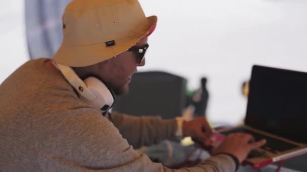 SOCHI, RUSIA - 1 DE ABRIL DE 2016: Dj en sombrero, gafas de sol girando en el tocadiscos en la estación de esquí. Auriculares. Cuaderno de notas — Vídeos de Stock