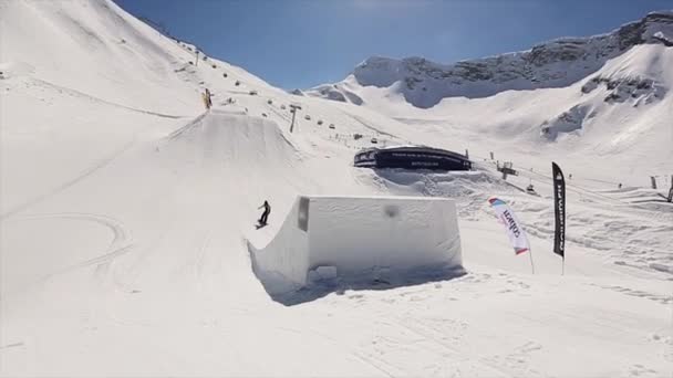 SOCHI, RÚSSIA - 1 de abril de 2016: Snowboarder jump from springboard. Paisagem de montanhas nevadas. Céu azul. Dia ensolarado. Pessoas — Vídeo de Stock