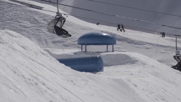 Ośrodek narciarski. Słoneczny dzień. Snowy góry. Narciarzy. Wyciągi narciarskie. Snowboardzistów. Niebieski trampoliny. — Wideo stockowe