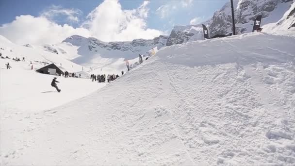 Soči, Rusko - 1. dubna 2016: Snowboardista jízdu na můstek udělat Salto ve vzduchu. Lidé. Sluneční svit. — Stock video