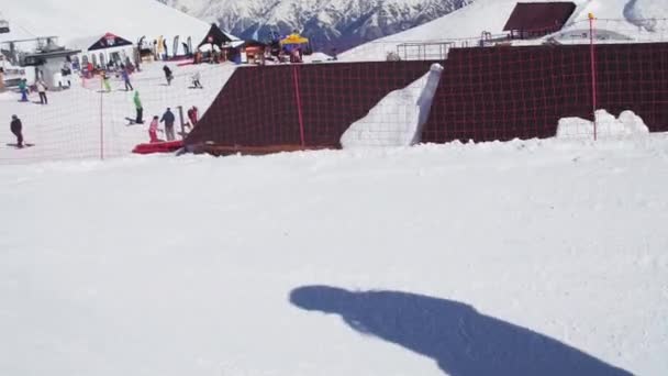 Sochi, Rusko - 2. dubna 2016: Lyžař jezdit na svahu, skok přes můstek. Sunny. Lyžařské středisko. Zasněžené hory. — Stock video