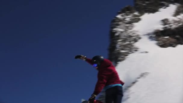 SOCHI, RUSIA - 1 DE ABRIL DE 2016: Salto snowboarder desde el trampolín hacer voltear en el aire, agarrar el tablero. Montañas nevadas. Día soleado. Cielo azul — Vídeos de Stock