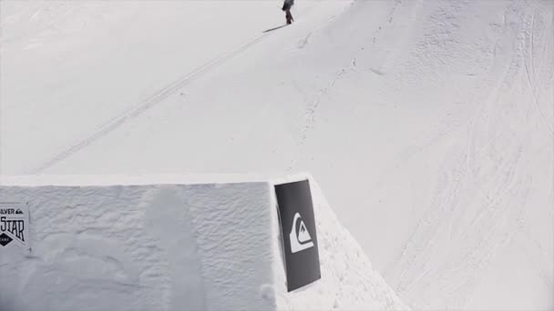 Sochi, Rusko - 1. dubna 2016: Snowboardista skok od odrazový můstek flip ve vzduchu. Zasněžené hory. Slunečný den. Modrá obloha. Aktivita — Stock video