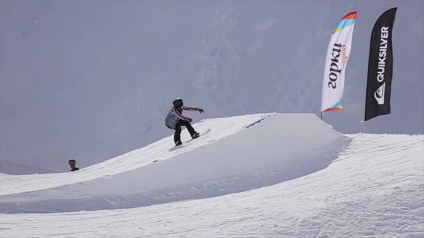SOCHI, RUSIA - 1 DE ABRIL DE 2016: Los snowboarders saltan desde el trampolín. Banderas. Estación de esquí. Montañas. Día soleado — Vídeos de Stock