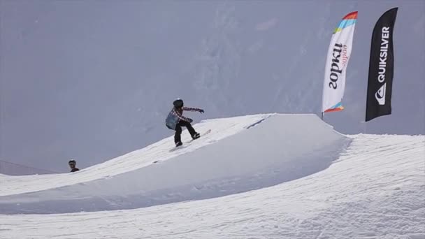 Soczi, Rosja - 1 kwietnia 2016: Skok wzwyż snowboardzistów z trampoliną. Flagi. Ośrodek narciarski. Góry. Słoneczny dzień — Wideo stockowe