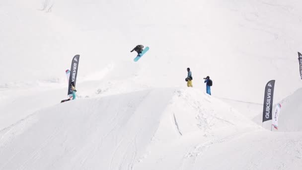 Sochi, Rusko - 1. dubna 2016: Snowboardista vysoký skok od odrazový můstek, jezdit na svahu. Lyžařské středisko. Lidé — Stock video