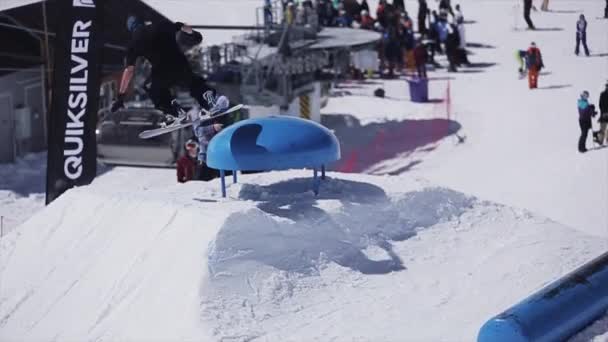 Sochi, Rusland - 2 April 2016: Snowboarder sprong over blauwe kicker. Zonnige dag. Skigebied. Besneeuwde bergen. — Stockvideo
