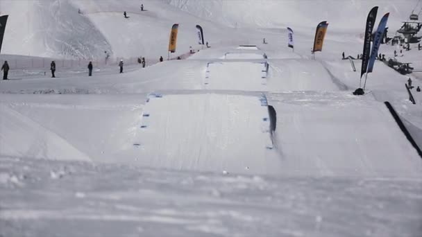 Sochi, Rusko - 1. dubna 2016: Snowboardista extrémní skok od odrazový můstek, chytit ve vzduchu. Zasněžené hory. Lyžařské středisko. — Stock video